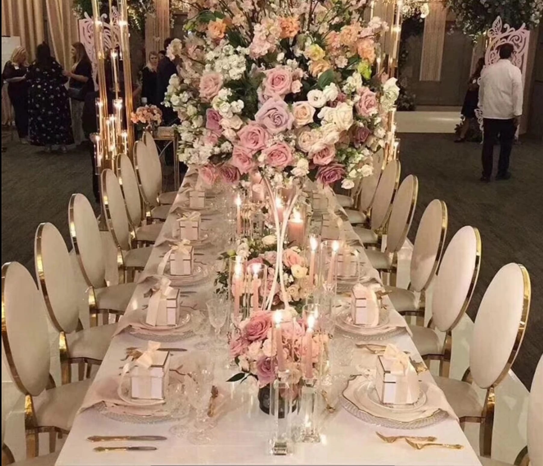 Long banquet table set with Classic Gold Circle chairs, blush pink and ivory floral centerpieces, gold-rimmed dinnerware
